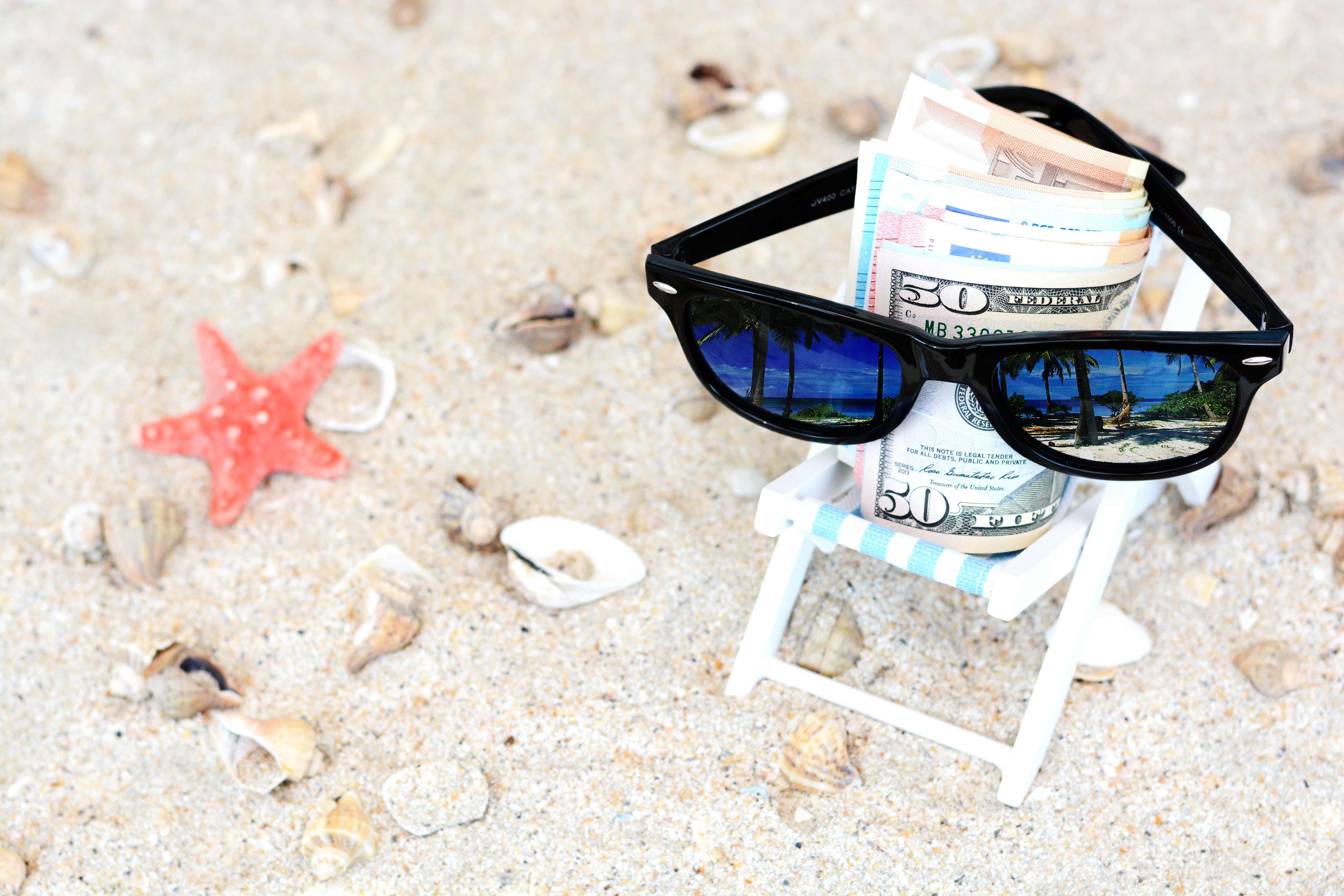 Holiday money concept - Banknotes with sunglasses in a beach chair and sand background